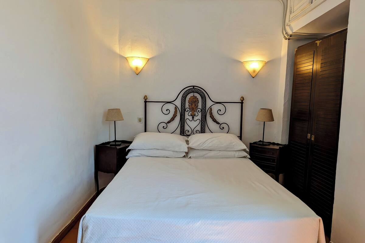 A neatly made bed with white linens, two bedside lamps, and a decorative headboard.