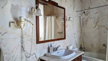 A bathroom with a marble wall, a wooden vanity, a sink, a mirror, and a shower.