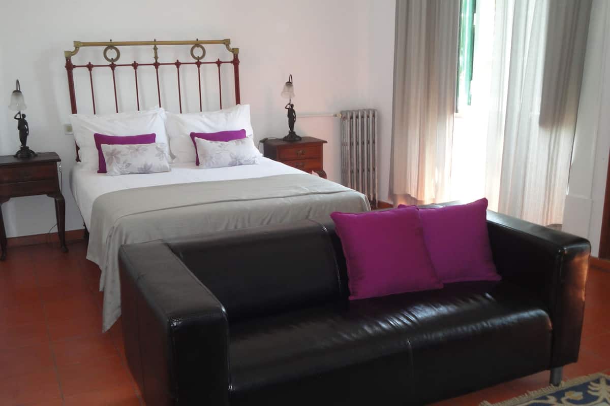 A bedroom with a bed, a black leather sofa, and a nightstand with a lamp.