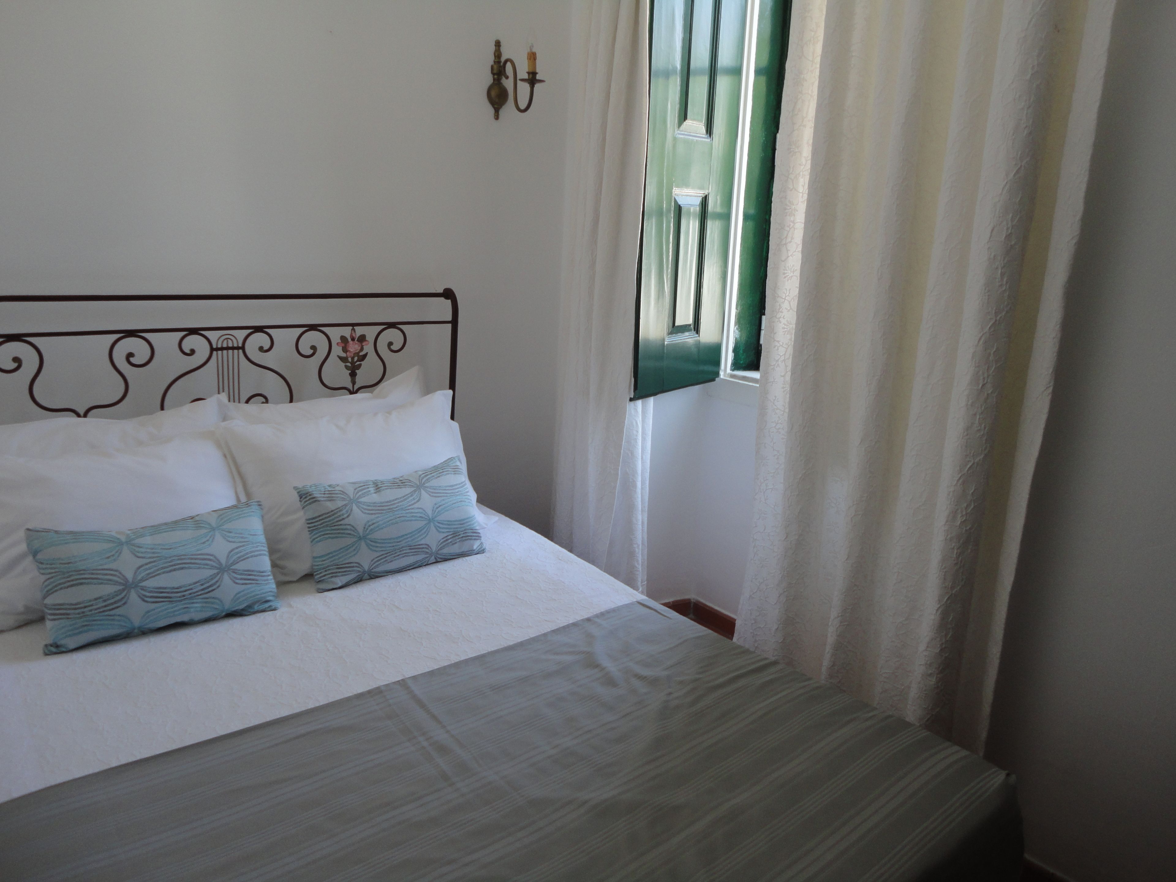 A neatly made bed with a patterned pillow, a metal headboard, and a window with curtains.