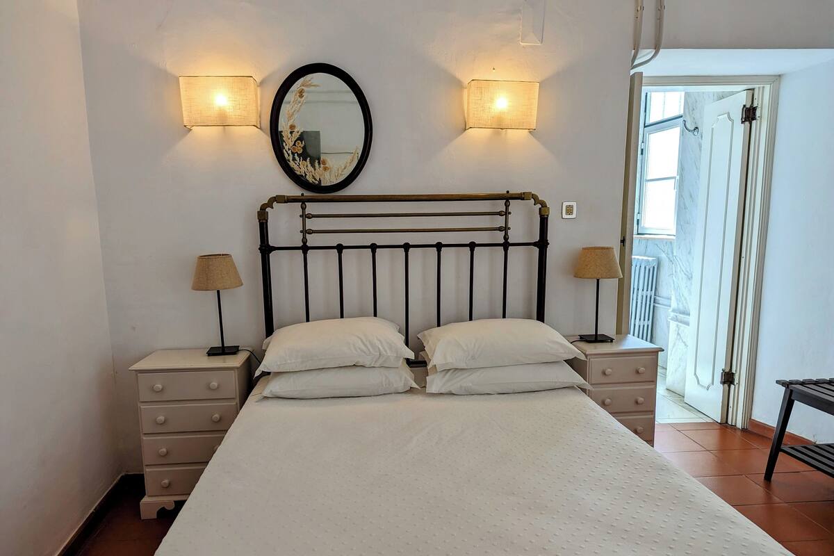 A bedroom with a bed, two bedside tables, a mirror, and two wall-mounted lamps.