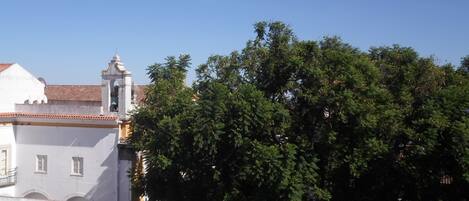 A building with a tiled roof, a bell tower, and a large tree in front.