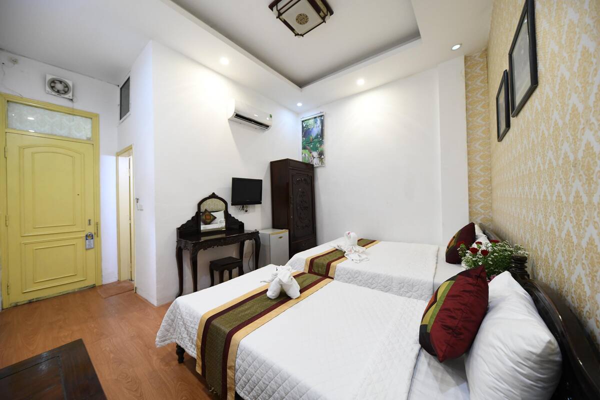 A hotel room with two beds, a desk, a wardrobe, and a small television.