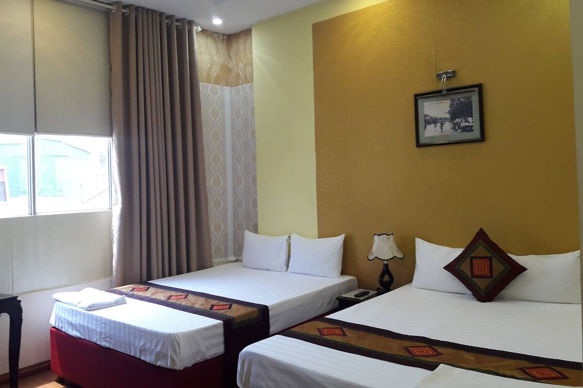 A hotel room with two single beds, a desk, a chair, a window with curtains, and a wall-mounted picture.