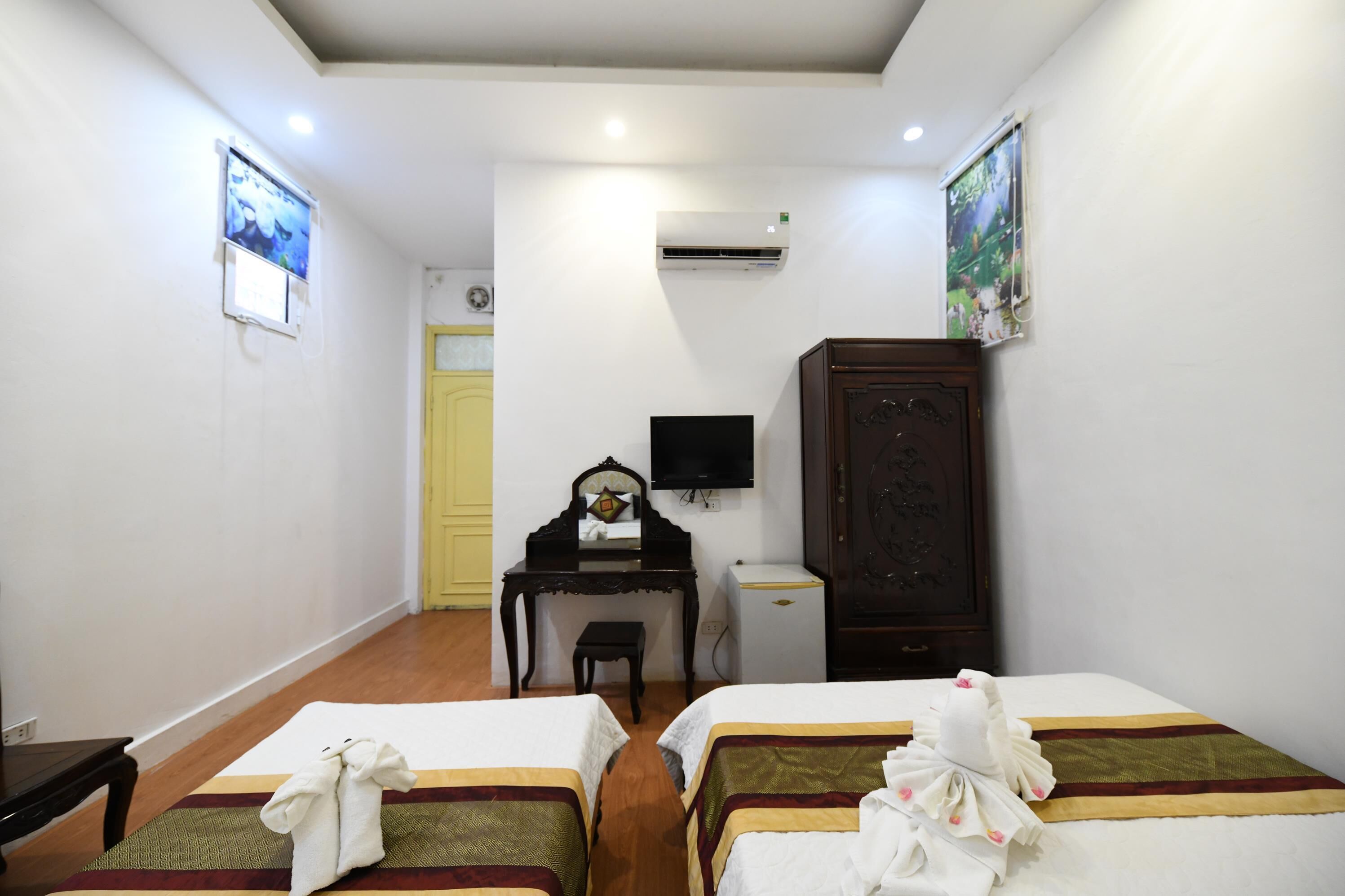A hotel room with two beds, a desk, a chair, a TV, an air conditioner, and a wardrobe.