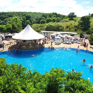 A swimming pool with a conical roof structure, surrounded by lounge chairs and umbrellas, set against a backdrop of lush greenery. - Bella Vista Beach Club (Tsarevo)