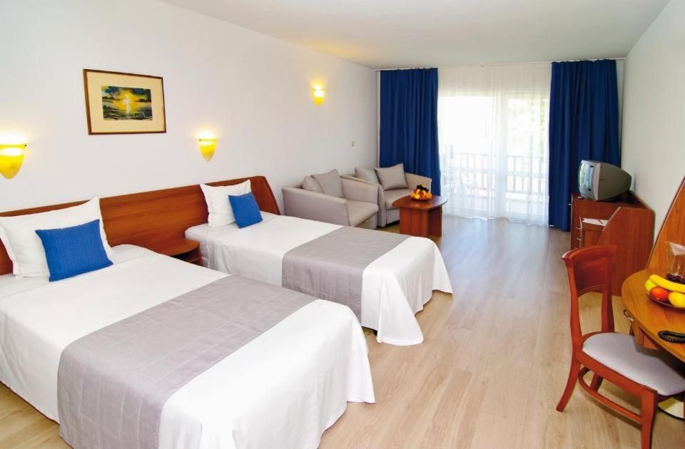 A hotel room with two beds, a sofa, a dining table with chairs, a TV, and a window with curtains.