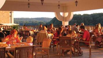 An outdoor dining area with multiple tables and chairs, surrounded by a covered structure with hanging lights.