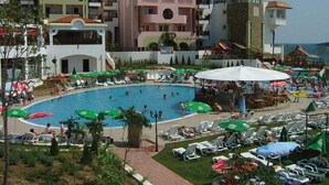 Ein Hotel mit Swimmingpool, umgeben von Liegestühlen und Sonnenschirmen, einem angelegten Garten und mehrstöckigen Gebäuden mit Balkonen.