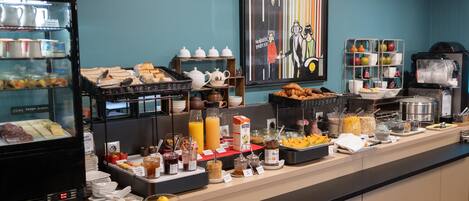 A buffet with various food items and beverages, including pastries, fruits, and condiments.