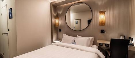 Quarto de hotel com uma cama grande, um espelho redondo, duas luminárias de parede, uma escrivaninha com cadeira e uma cafeteira.