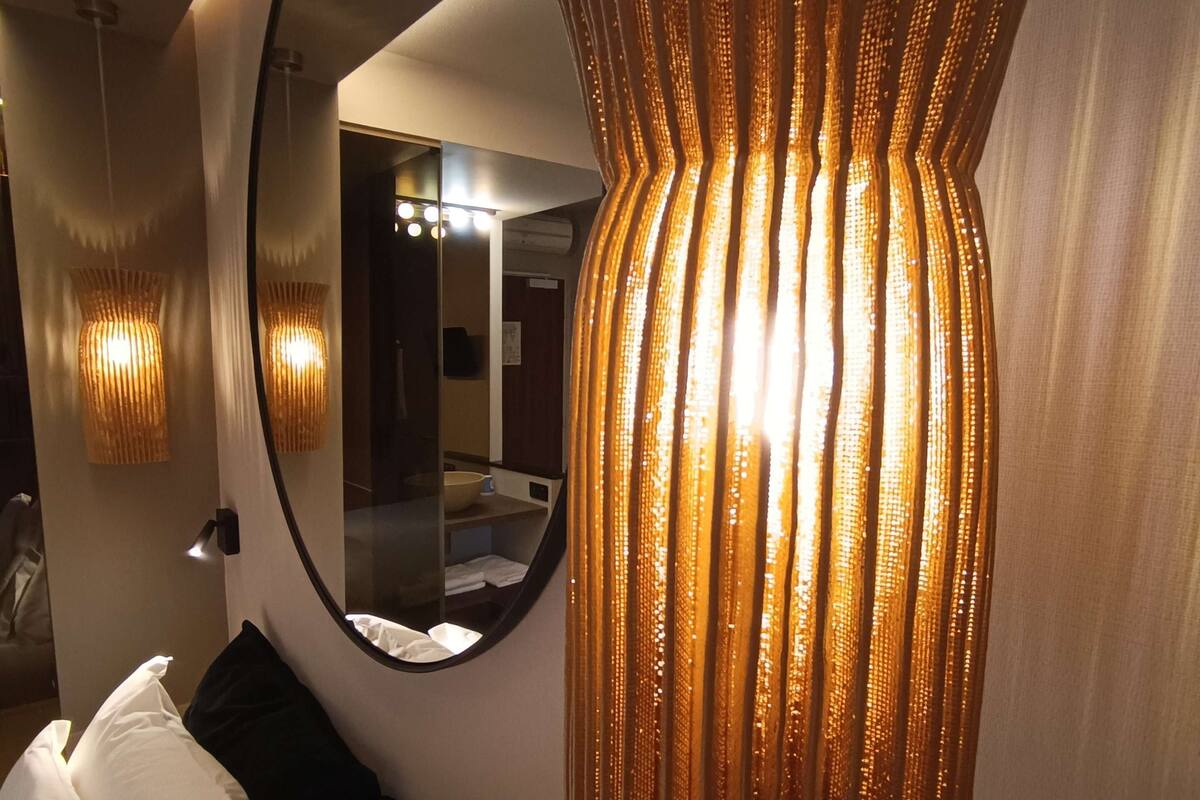 Une chambre d’hôtel moderne, dotée d’un grand miroir, d’un luminaire au design original et d’un lit parfaitement fait.