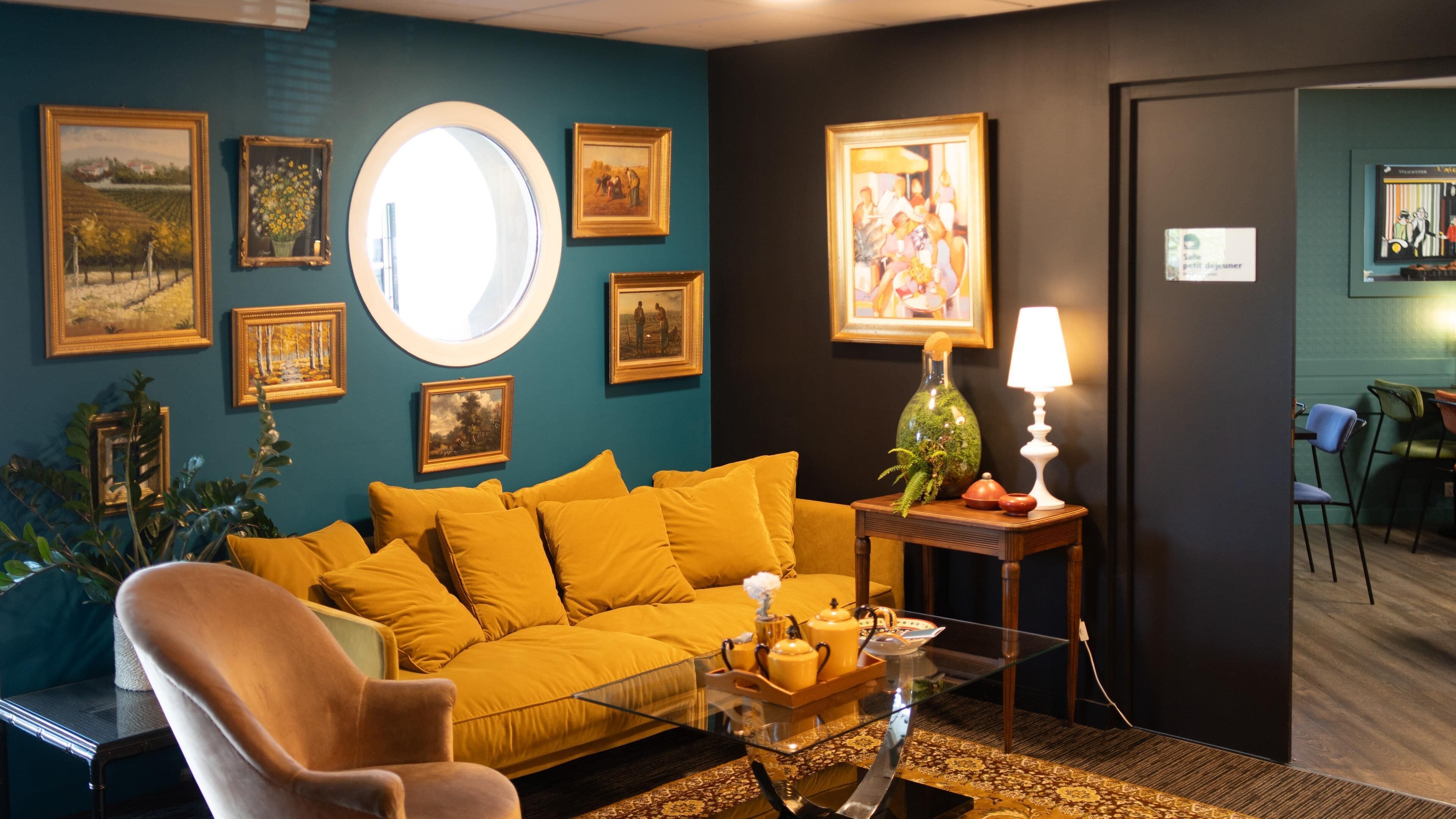 A room with a yellow sofa, a round mirror, and various framed artworks on the walls.