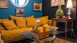 Una sala de estar con un sofá amarillo, una mesa de centro de vidrio con teteras amarillas y cuadros en la pared.