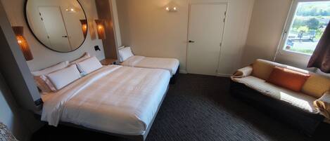 Habitación de hotel con dos camas, un sofá, un espejo grande y una ventana con vistas.