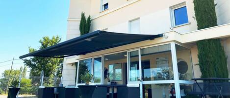 A hotel exterior with a covered outdoor seating area, a sign reading "Kyriad Hotel," and a drive-through window.