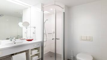 Un baño moderno con ducha envuelta en cristal, un espejo grande, un lavamanos con un jabonera roja y un inodoro.