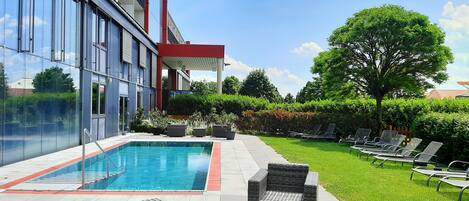 A modern building with a swimming pool, outdoor seating, and a well-maintained lawn.