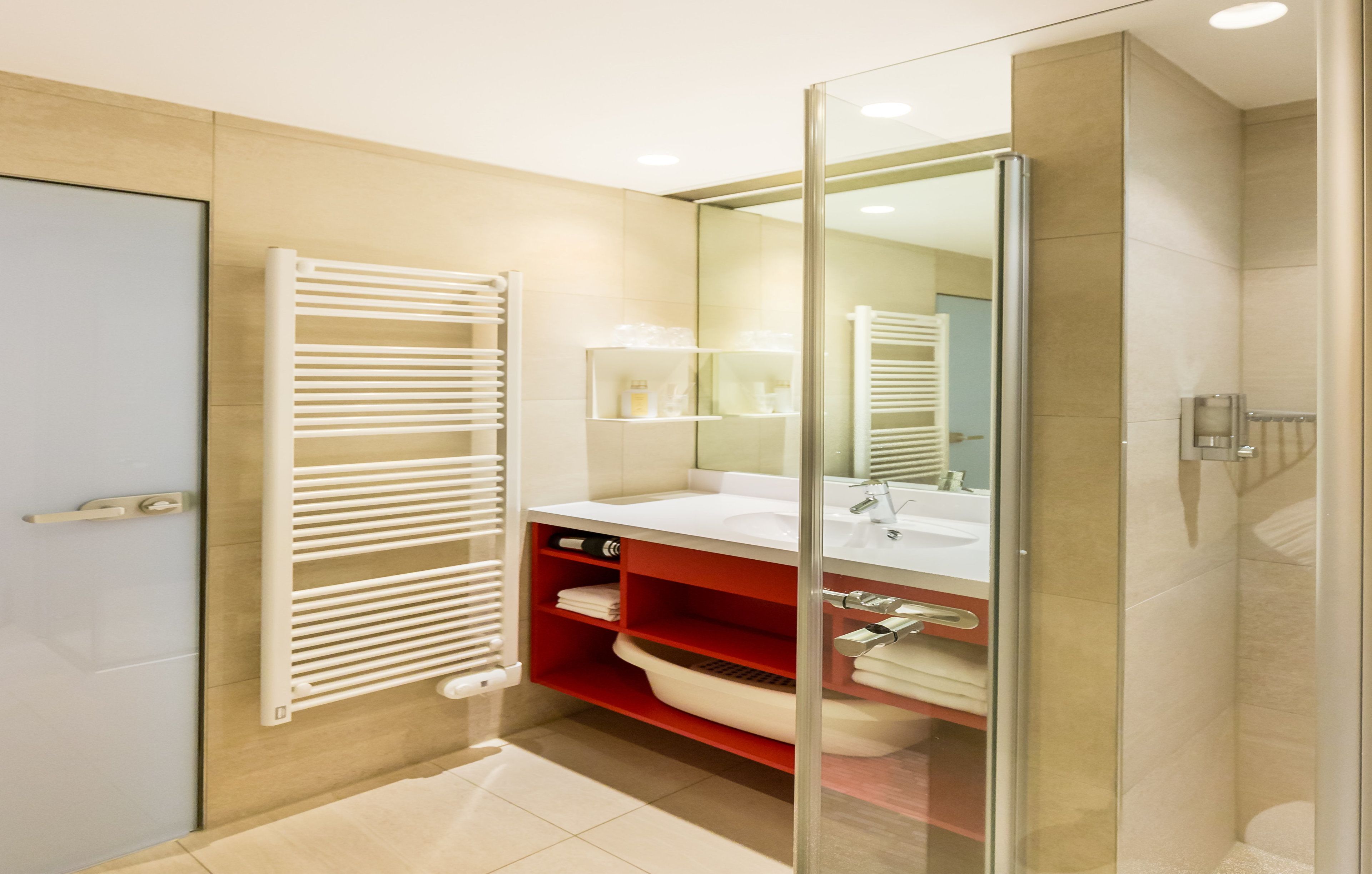 Un baño moderno con cabina de ducha de vidrio, un lavabo blanco y un estante rojo.