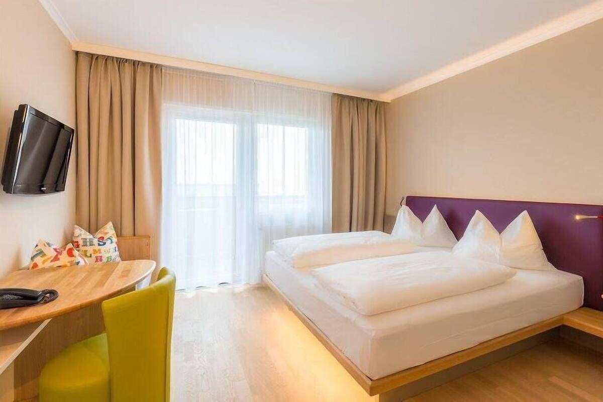 A hotel room with a bed, a desk, a chair, and a television.