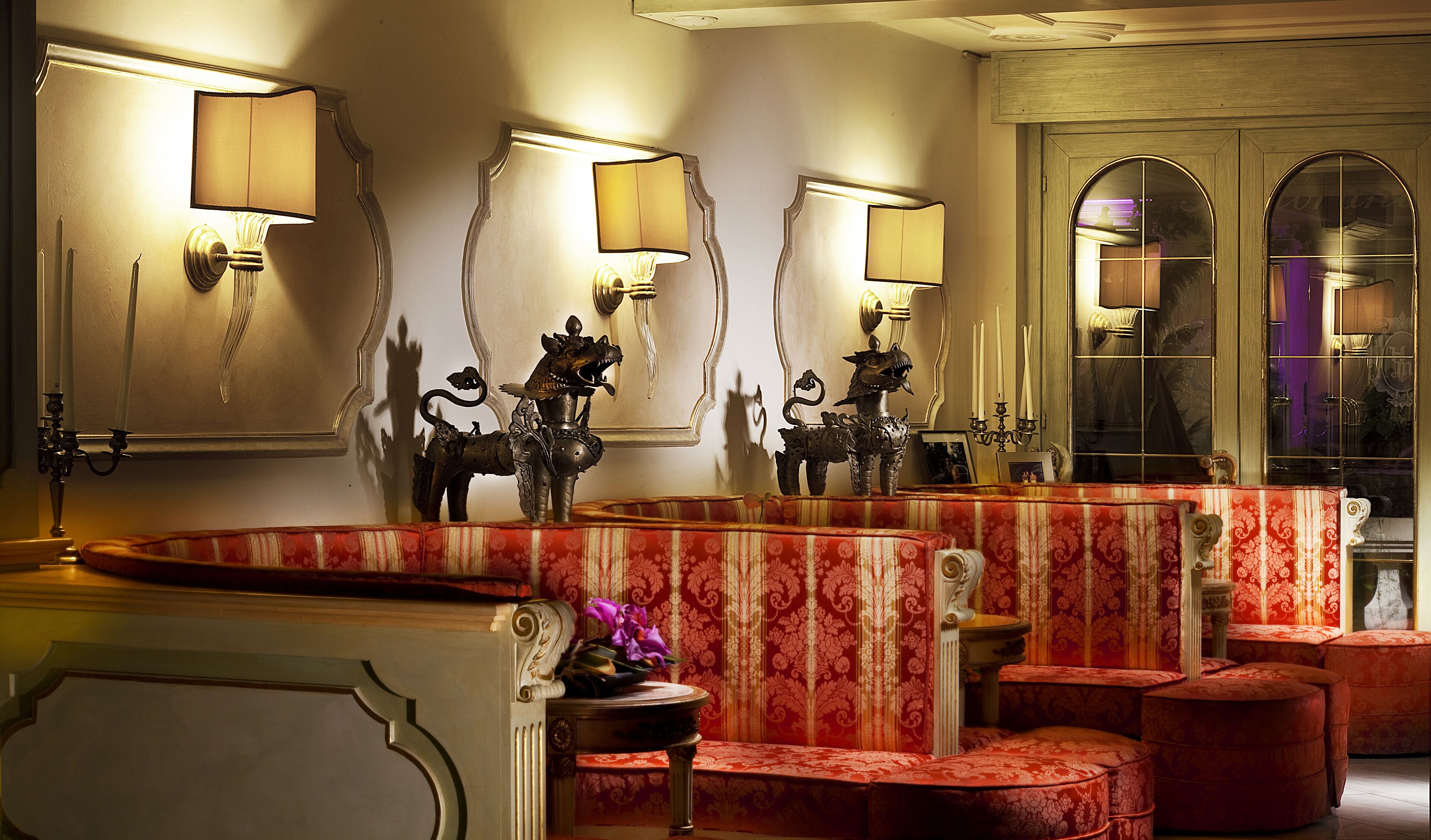 A luxurious room with ornate wall sconces, a large mirror, and a red patterned sofa.