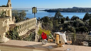 A terrace with a view of a lake, a statue, and a table with wine glasses and a pitcher. - Park Hotel Ville Montefiori (Gardone Riviera)