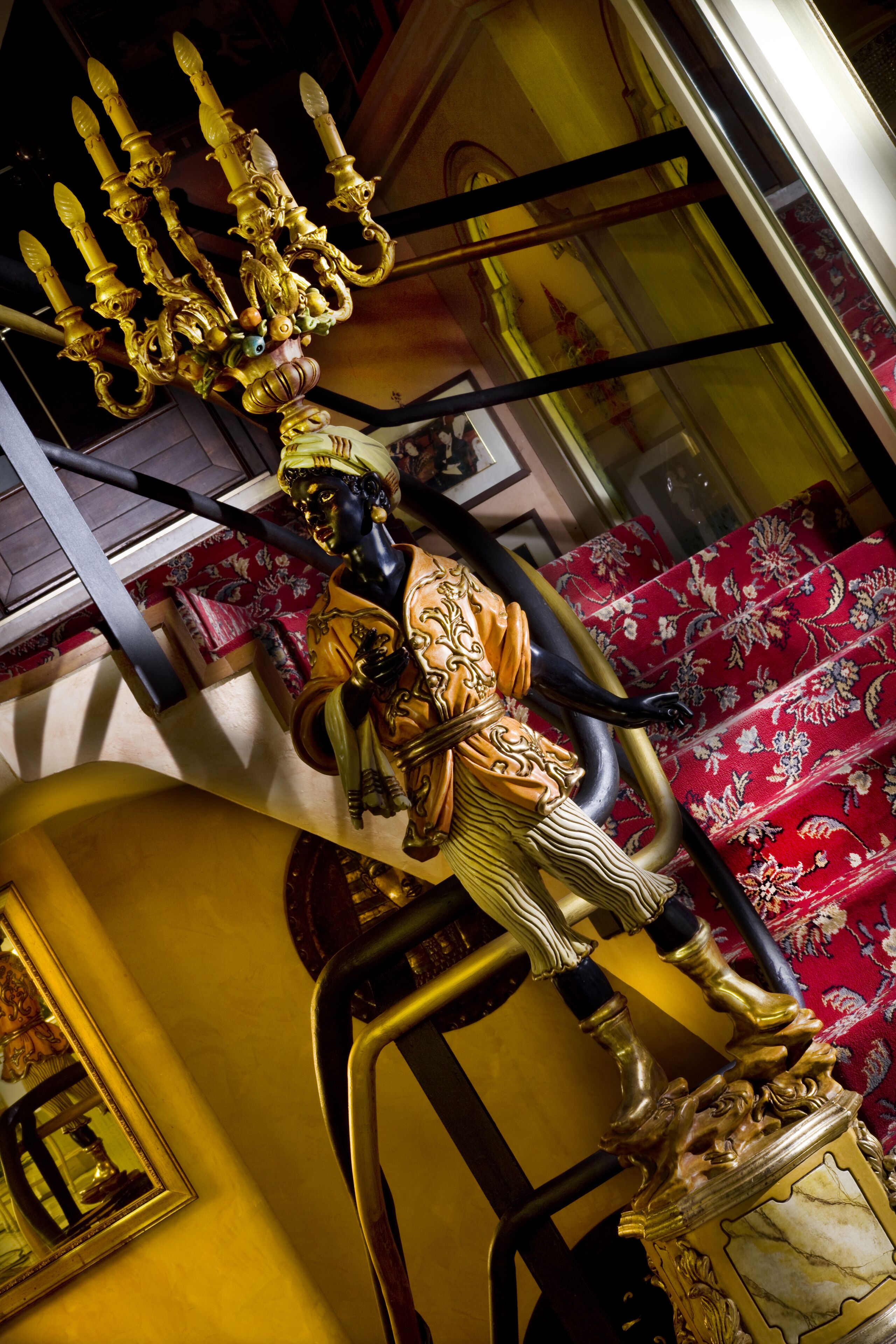 A golden candelabra with intricate designs, a red patterned carpet, and a wooden chair.