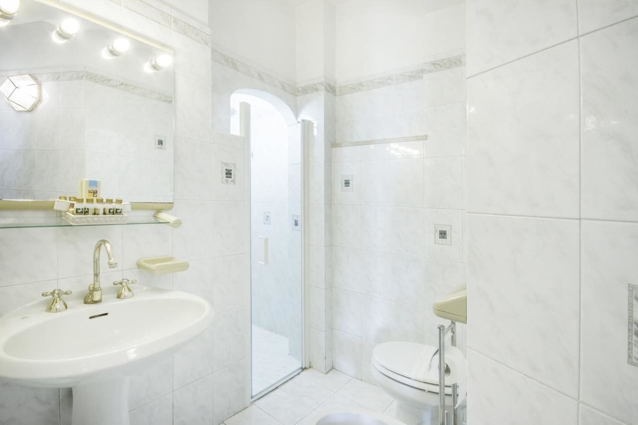 A bathroom with a white sink, mirror, and toilet. There is a glass shower door and a tiled floor.