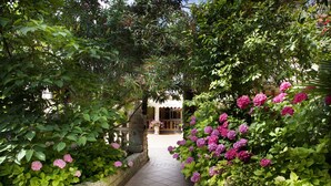 A pathway flanked by lush greenery and flowering plants leading to a building with a tiled entrance. - Park Hotel Ville Montefiori (Gardone Riviera)