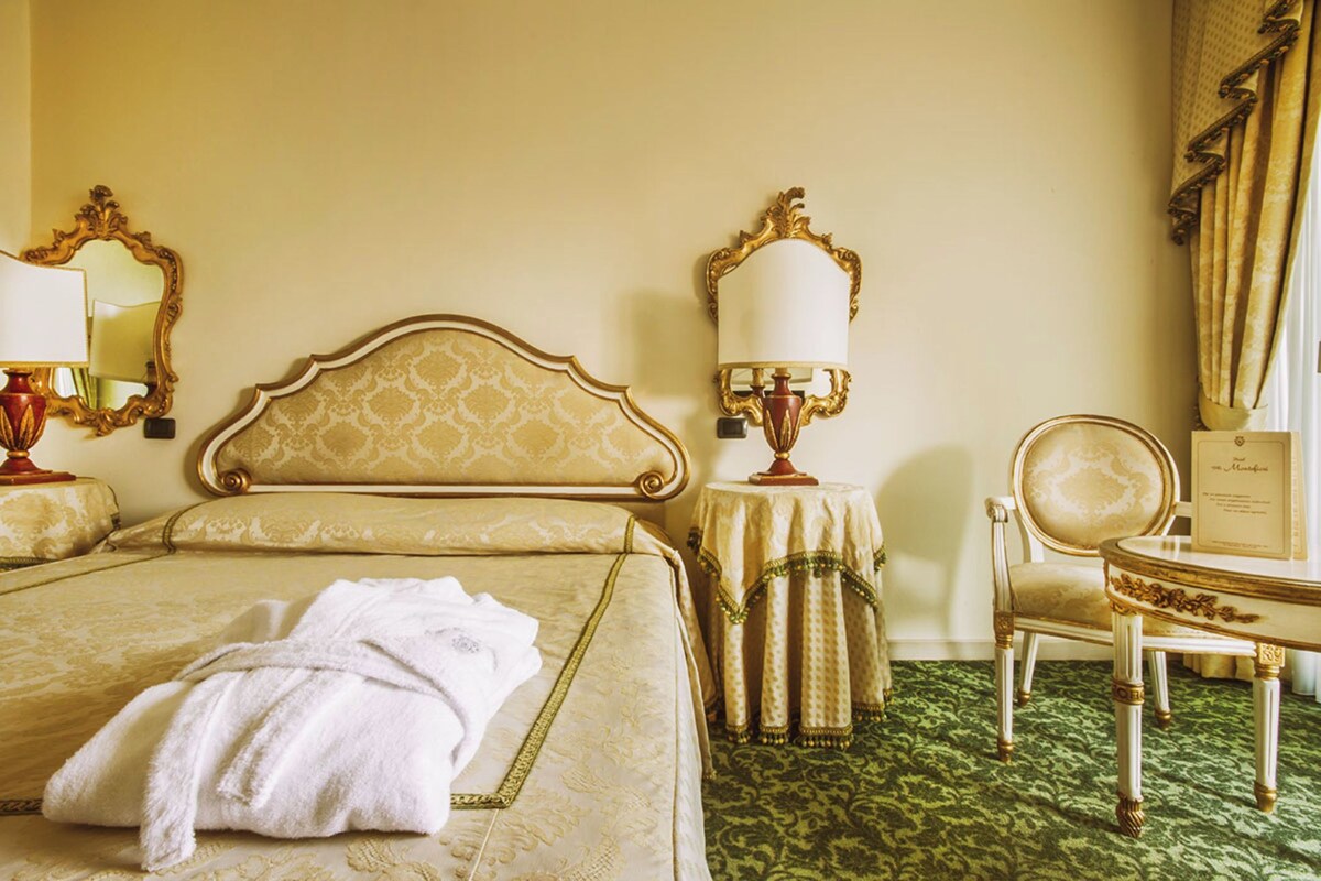 A hotel room with a large bed, two bedside tables, a chair, and a small table with a lamp.