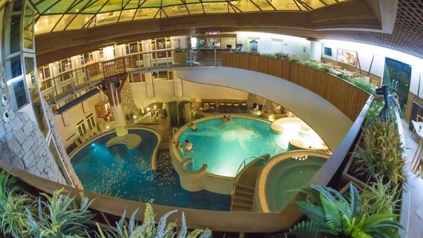 An indoor swimming pool with multiple levels, surrounded by plants and wooden railings. - MenDan Magic Spa & Wellness Hotel (Zalakaros)