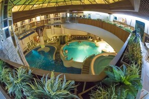 An indoor swimming pool with multiple levels, surrounded by plants and wooden railings. - MenDan Magic Spa & Wellness Hotel (Zalakaros)