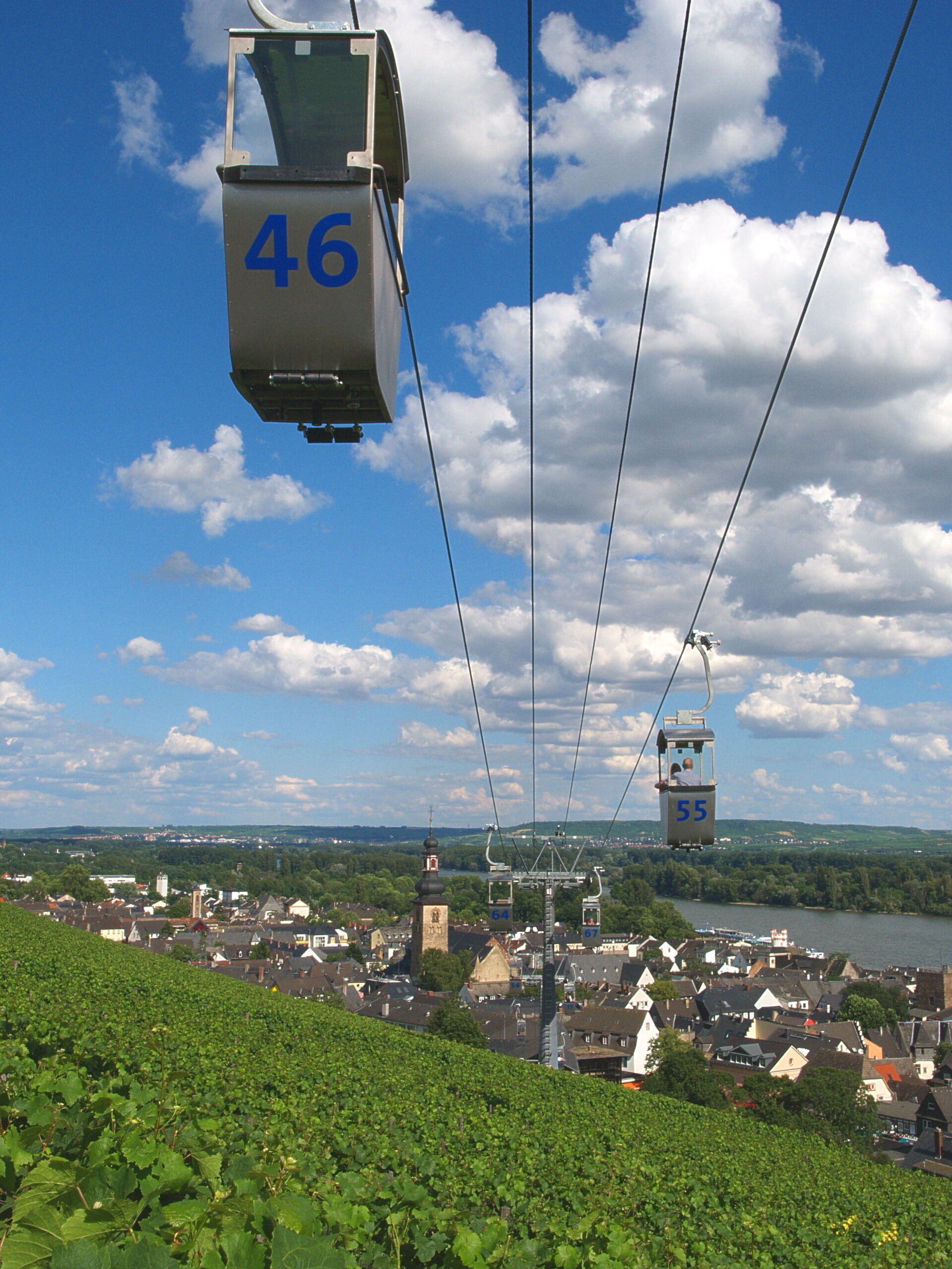 Un réseau de téléphériques composé de cabines numérotées 46 et 55, une ville avec un imposant beffroi, et une rivière en arrière-plan.