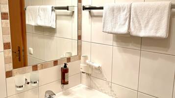 Baño con lavamanos blanco, espejo, toallero con dos toallas, secador de pelo y jabón de manos.