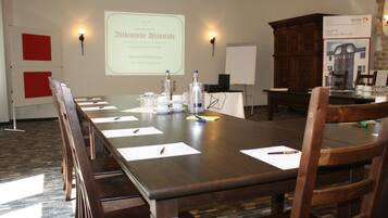 A conference room with a long table, chairs, a projector screen, and a wooden cabinet.