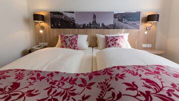 A hotel room with two beds, a nightstand with a phone, and a wall-mounted lamp.