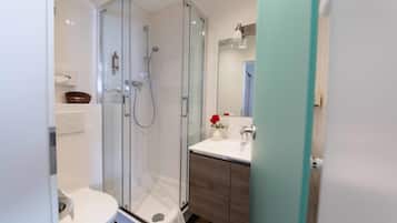 Un baño moderno con ducha envuelta en vidrio, inodoro blanco y tocador con espejo.