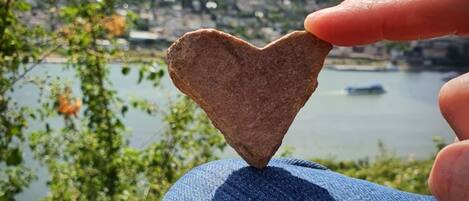 A heart-shaped stone held by a hand against a scenic backdrop of a lake and city.