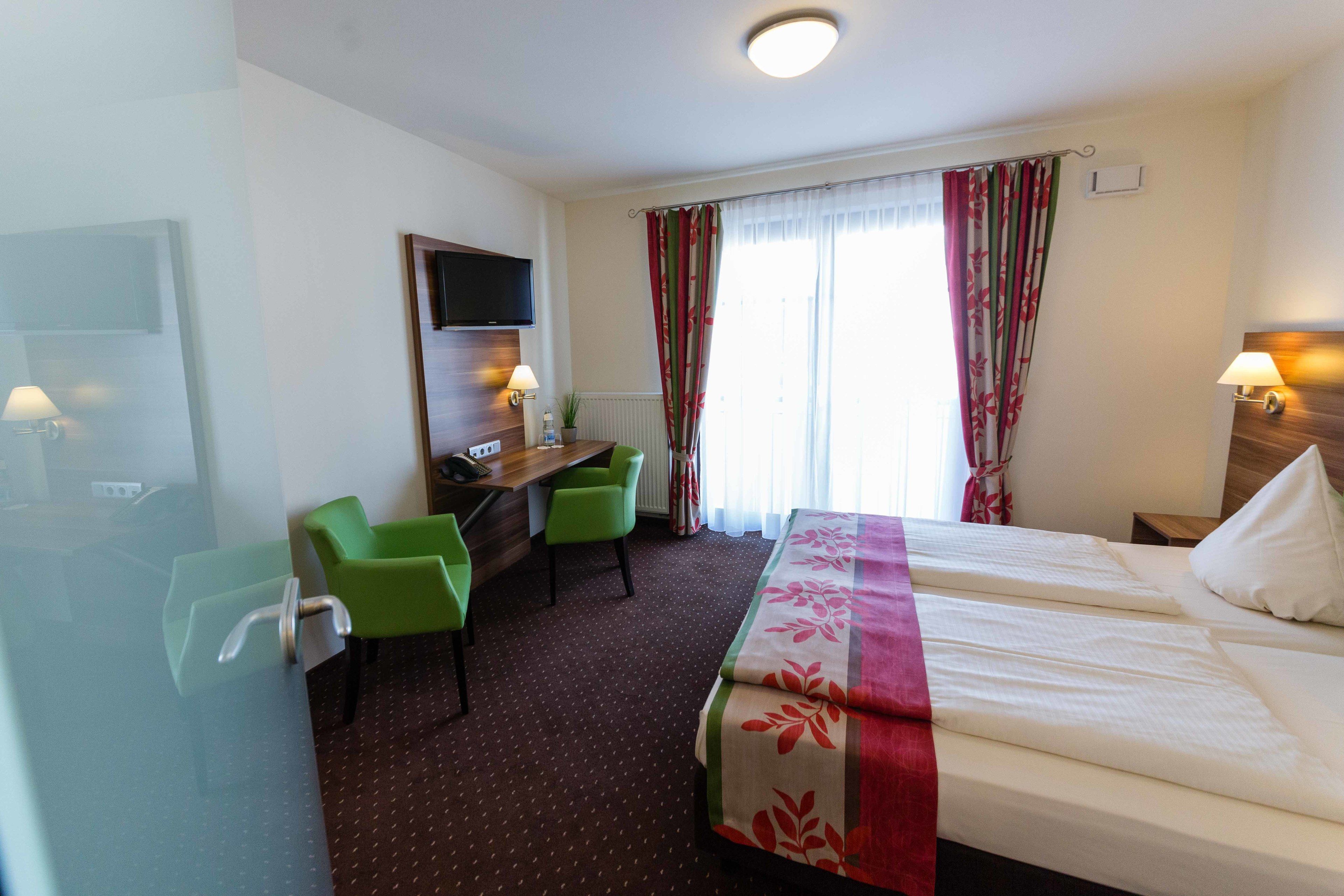 A hotel room with two beds, a desk with a chair, a TV, and a window with curtains.