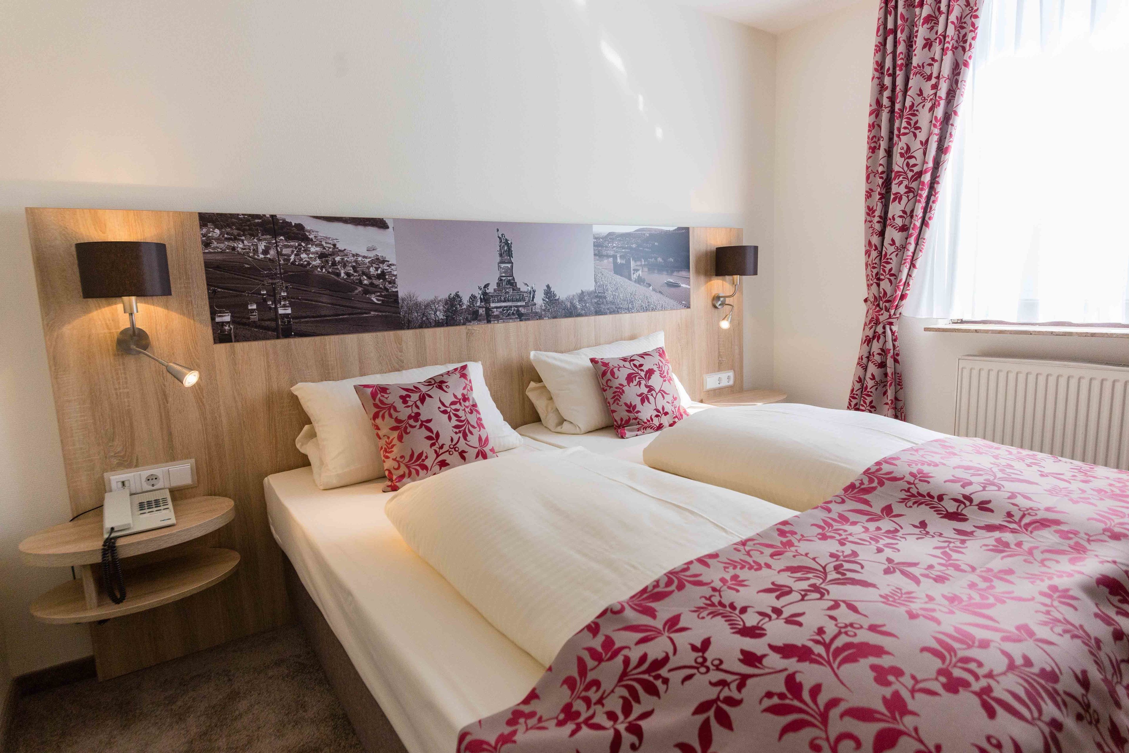 Una habitación de hotel con una cama grande, dos mesitas de noche, una lámpara de pared, un teléfono y una ventana con cortinas.