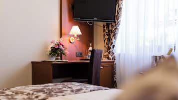 Une chambre d’hôtel avec un lit, un bureau avec une lampe, une télévision et une fenêtre avec des rideaux.