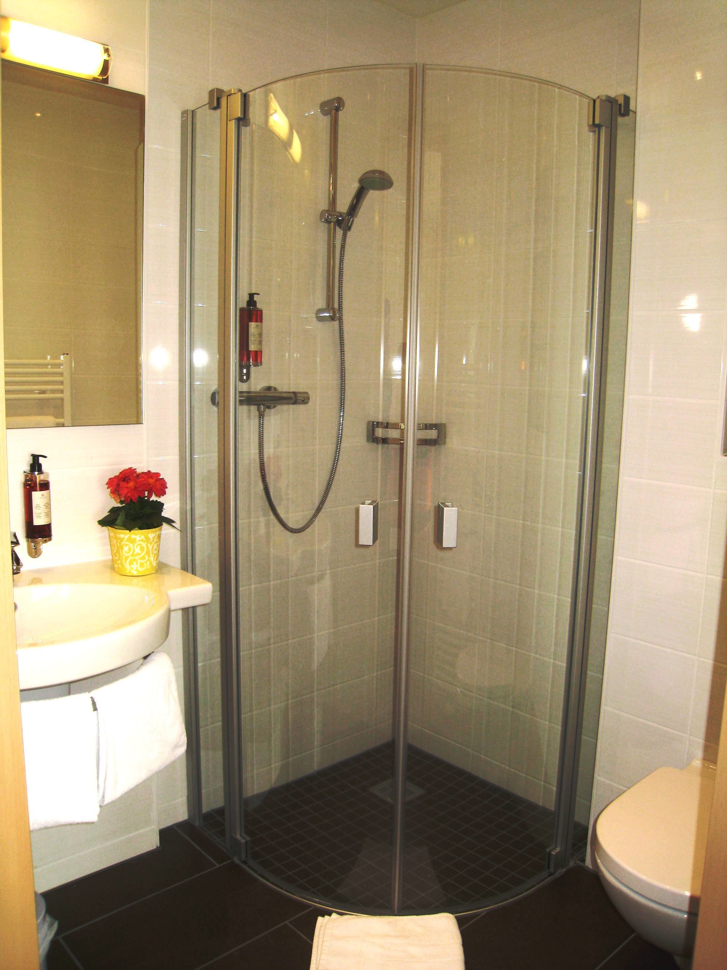 Eine Dusche mit Glaswand, Handbrause und separatem Wasserhahn.