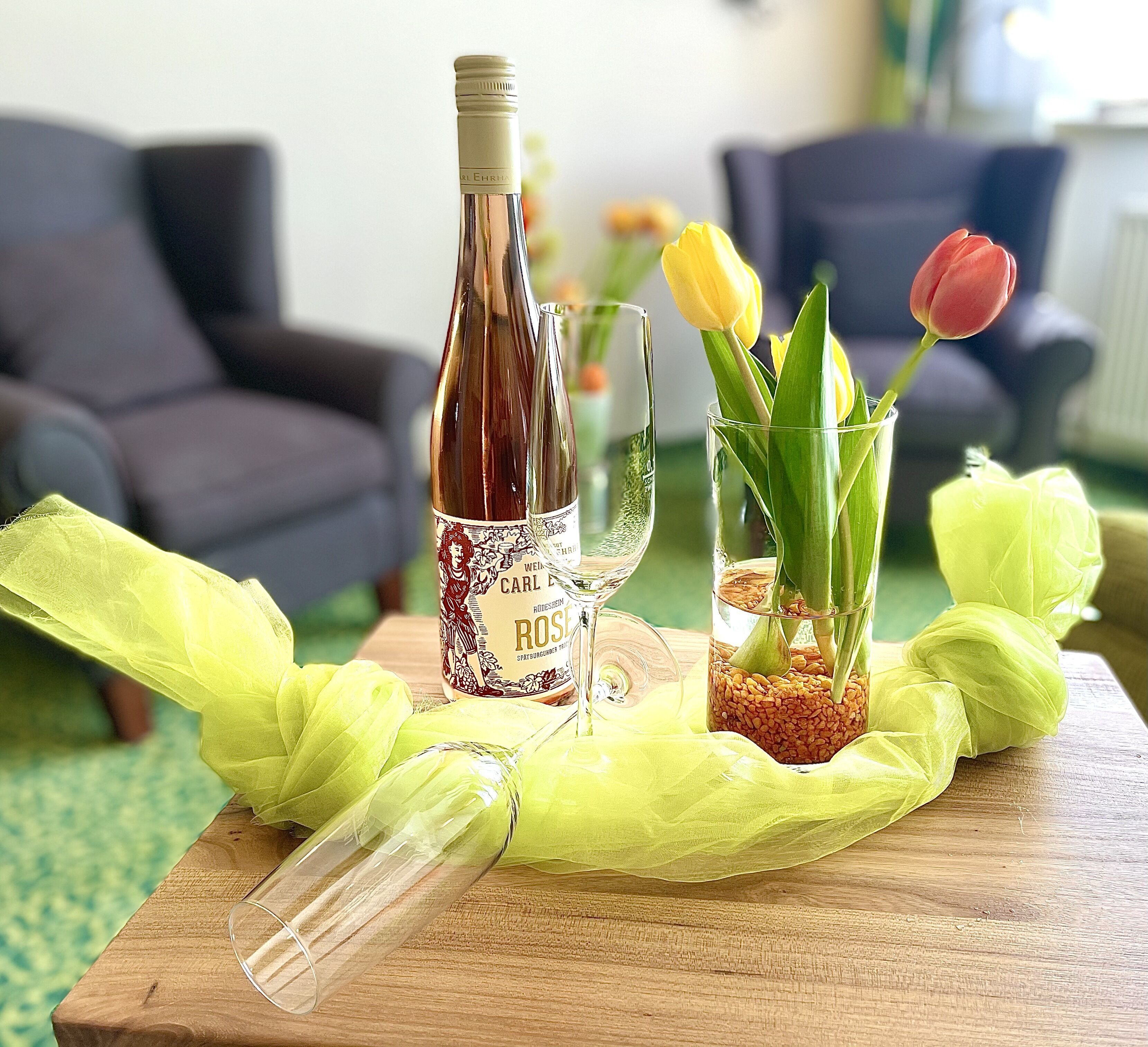 A bottle of wine, a glass, and a tulip on a wooden table.