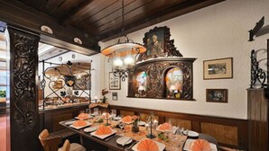 A dining area with a long table set for a meal, featuring a chandelier and ornate wall decorations. - Altdeutsche Weinstube (Ruedesheim am Rhein)