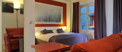 A modern hotel room with a bed, red sofa, and a table.