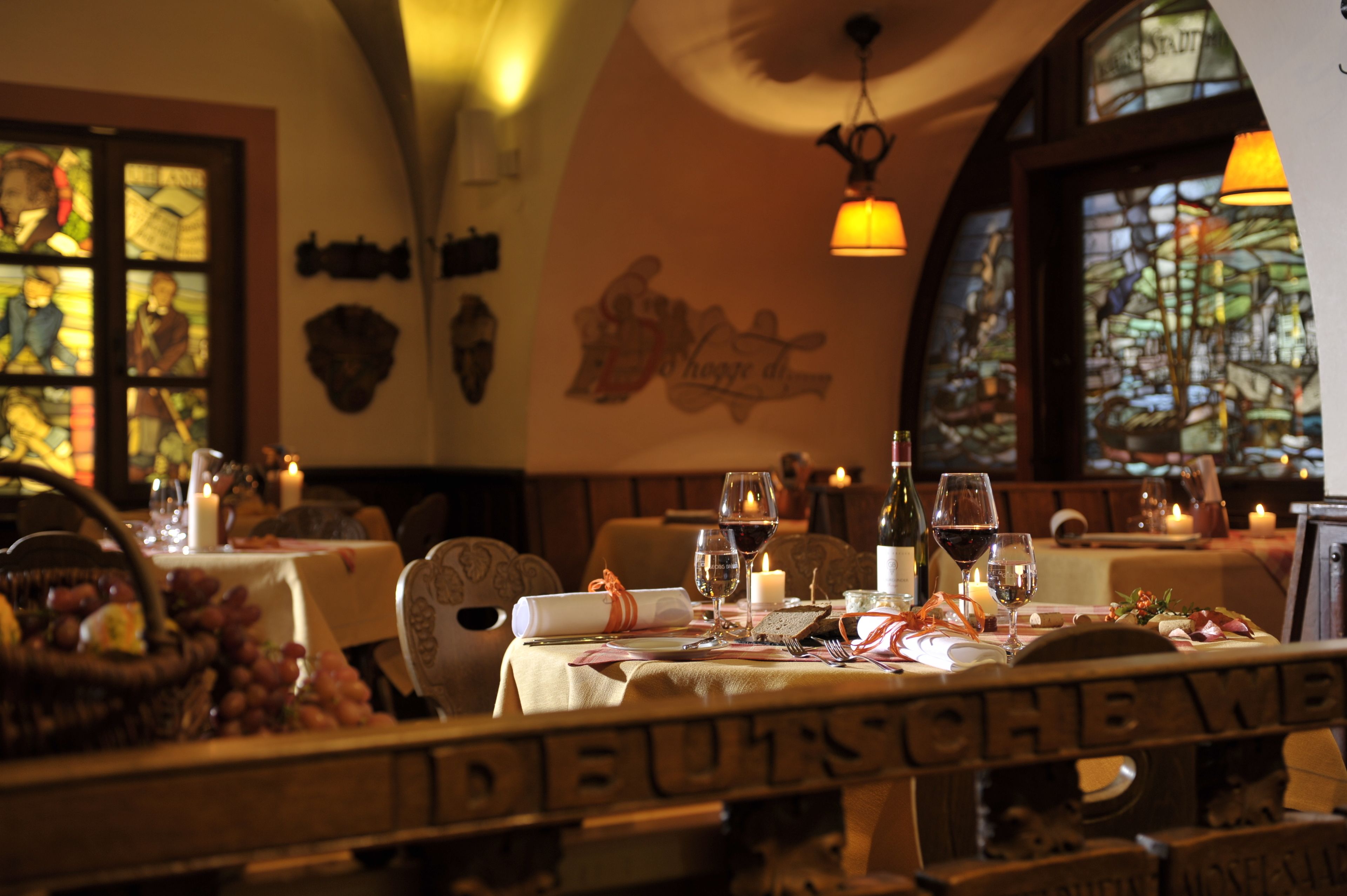 A restaurant interior with tables set for dining, featuring a chandelier and stained glass windows.