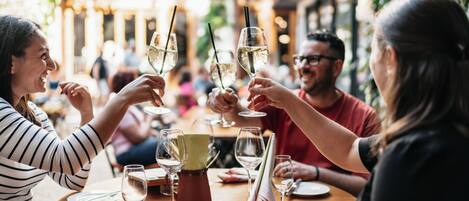 A group of people toasting with champagne glasses at a wooden table in an outdoor dining area with a warm, inviting atmosphere.