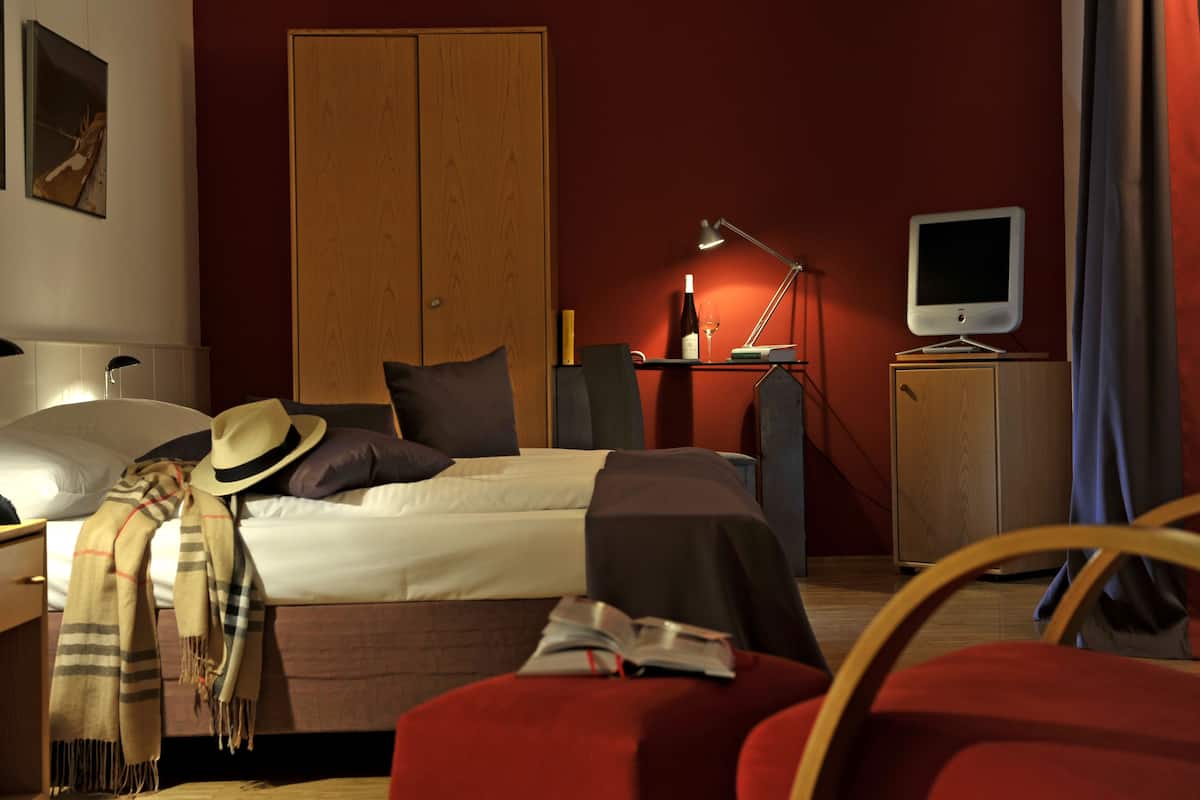 A hotel room with a bed, a desk with a lamp, a television, and a wardrobe.