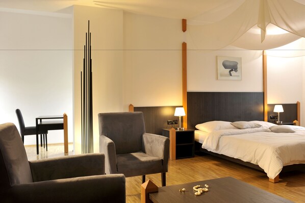 A hotel room with a bed, two bedside tables with lamps, a chair, a small table with decorative items, and a tall, modern light fixture.