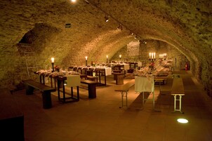 Un comedor subterráneo con paredes de piedra, mesas y bancos de madera, y mesas iluminadas con velas.